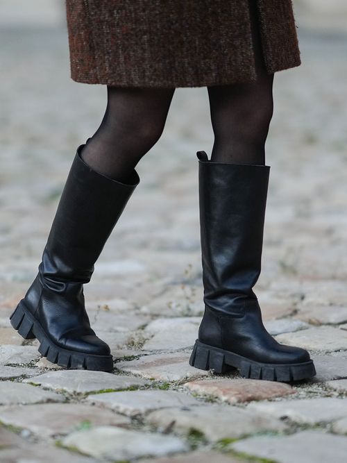 Close up von Beinen mit einer schwarzen Strumpfhose, einem grauen Mantel und kniehohen Chunky Boots.