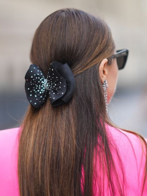 Julia Comil trägt einen pinken Blazer und eine Haarklammer-Schleife als Frisur.