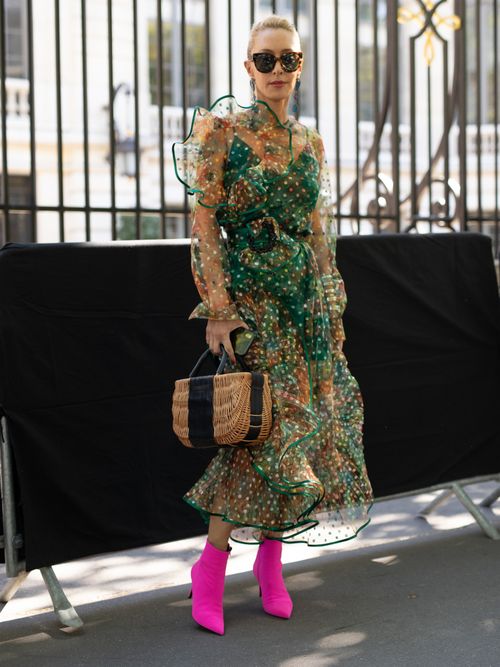 Street Style Look von der Paris Fashion Week, wo ein Gast ein grünes Blumenkleid trägt, dazu pinke Schuhe und einer Strohtasche.