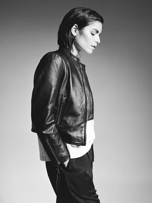 Frau mit kurzer Lederjacke, weißem T-Shirt und schwarzer Hose.