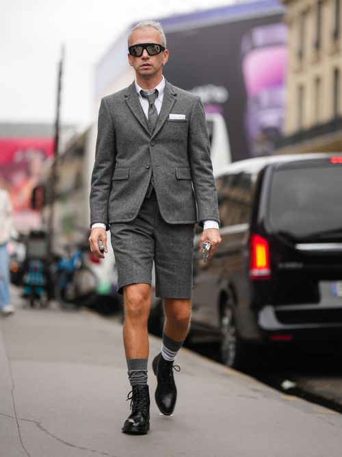 Street Style Look von der Paris Fashion Week, wo ein Gast einen grauen Anzug mit passender kurzer Shorts und weißem Hemd mit Krawatte trägt.