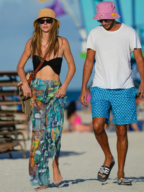 Seyma Subasi trägt ein schwarzes Crop Top mit buntem Wickelrock, Umhängetasche und Bucket Hat auf dem Strand von Miami.