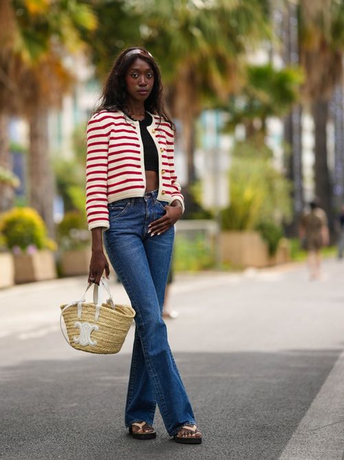 Emmanuelle Koffi wears a Celine red and white stripe cardigan with jeans, straw bag, and flip flops