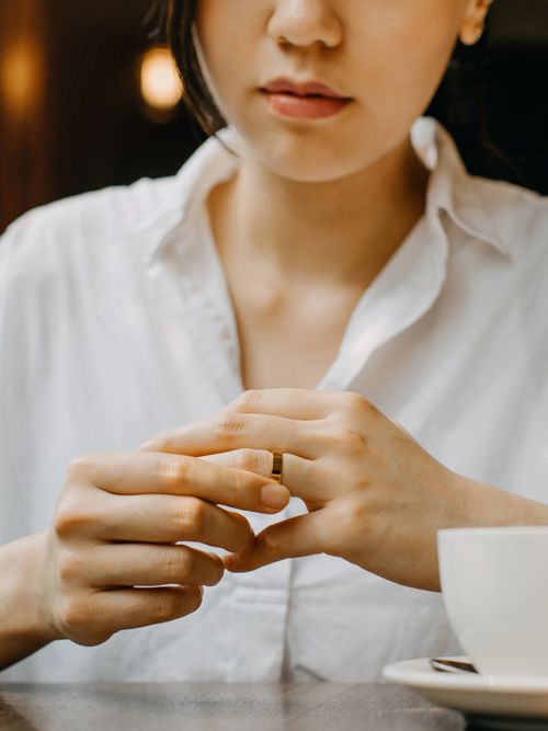 Eine Frau sitzt im Kaffeehaus und versucht sich den Ring vom Finger zu nehmen.