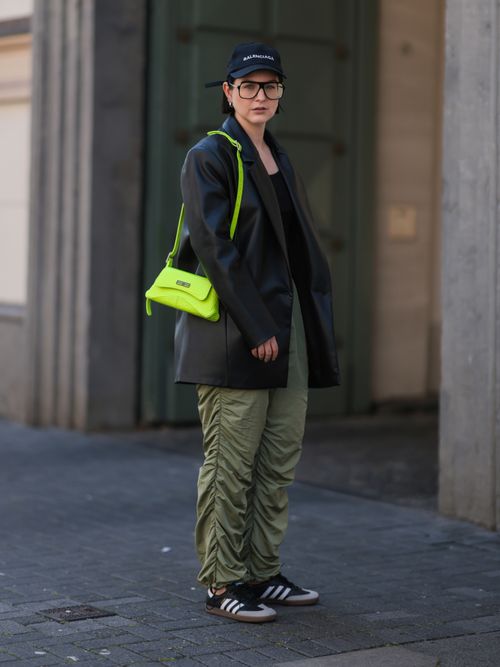 Maria Barteczko trägt einen Lederblazer mit grüner Hose und gelber Tasche, sowie Adidas Samba Sneaker in Düsseldorf.
