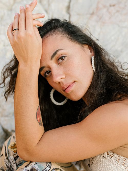 Frau mit gehäkeltem Oberteil und weißen Creolen greift sich an den Kopf.