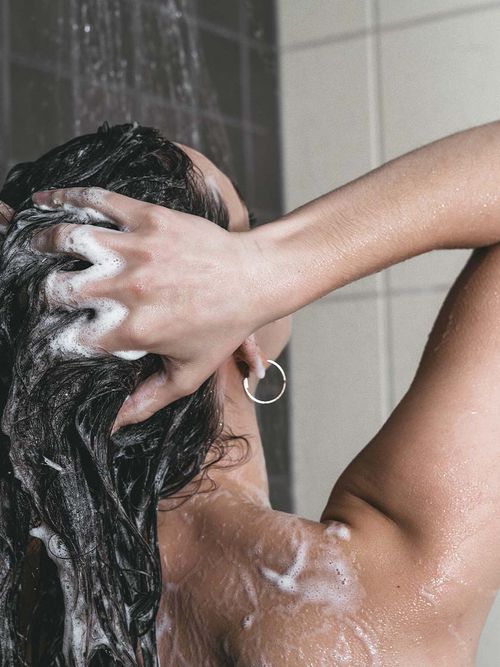 Frau unter der Dusche, die sich gerade die Haare wäscht.