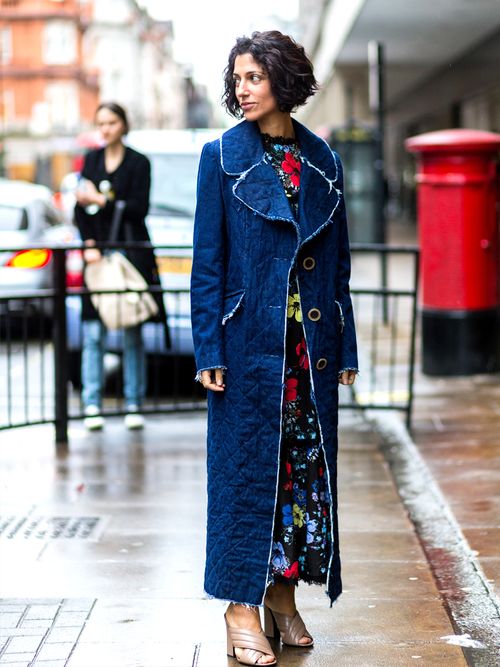 A street style photo of a woman wearing a floral maxi dress and a denim duster.