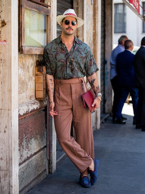 Kadu Dantas trägt eine Kurzarmhemd mit Tropcialprint, dazu eine braune Leinenhose, mit Hut und Sonnenbrille auf der Milan Fashion Week.