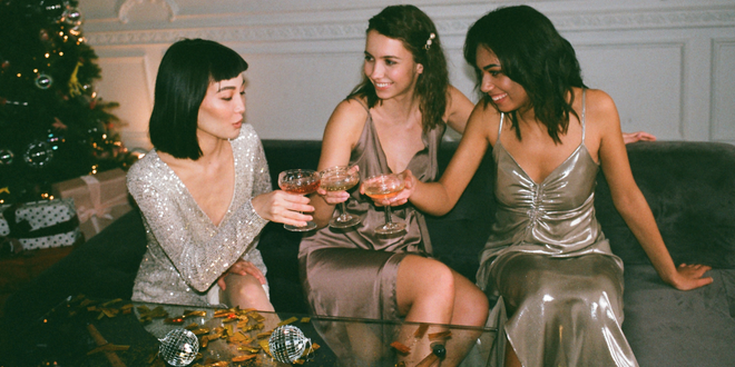 Drei Frauen in festlicher Partykleidung stoßen an.