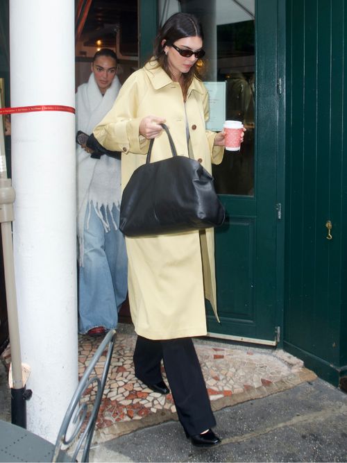 Kendall Jenner is seen on September 18, 2023 in New York City wearing sunglasses, a yellow trench coat, black pants, black leather shoes, and a black leather tote bag.