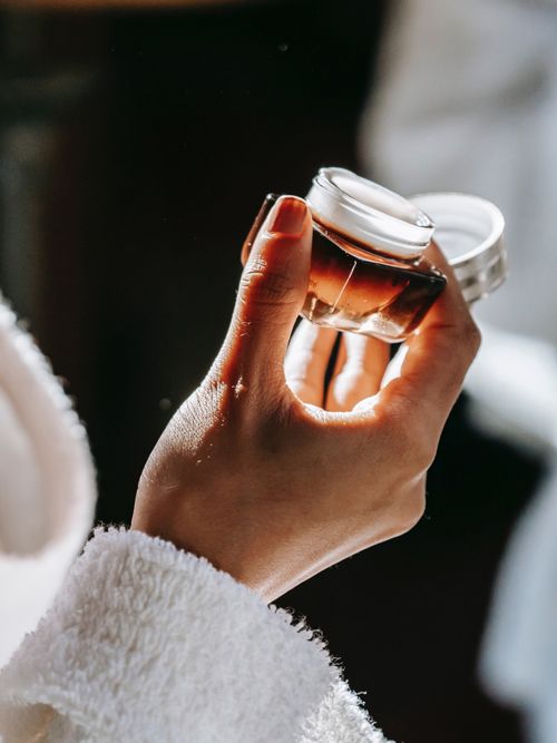 Frauenhände die eine braune Cremedose in der Hand halten.