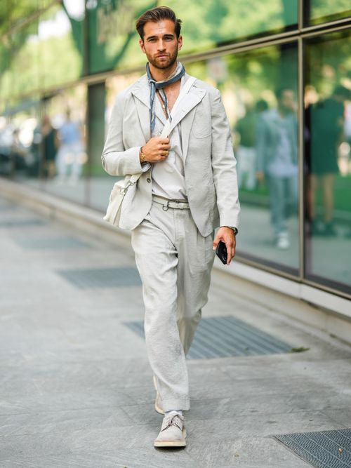 Daniel Toni Jais trägt einen hellgrauen Leinenanzug mit weißem Hemd, weißer Umhängetasche und Halstuch auf der Milan Fashion Week.