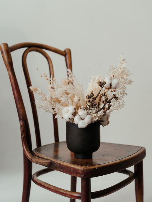 Ein Strauß mit Trockenblumen steht auf einem braunen Holzstuhl.