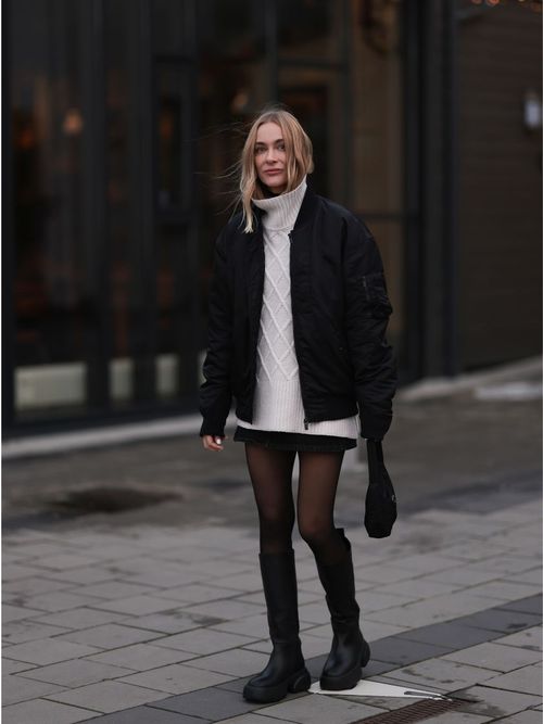 Marie Hindkaer trägt eine schwarze Bomberjacke, ein kurzes Strickkleid mit Minirock und schwarzen Stiefel in Reykjavik