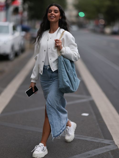 Street Style Look aus Düsseldorf, wo eine Influencerin einen Jeansrock mit weißen Sneakers und eine weiße Bomberjacke trägt.
