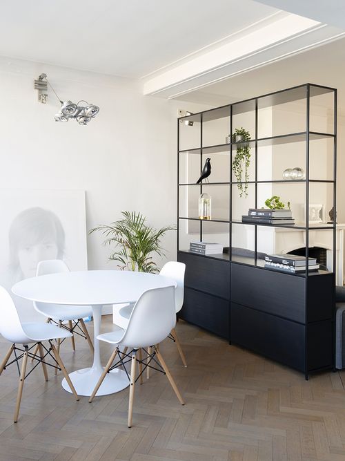 Esszimmer mit einem runden weißen Esstisch, weißen Eames Stühlen und einem schwarzen Regal.