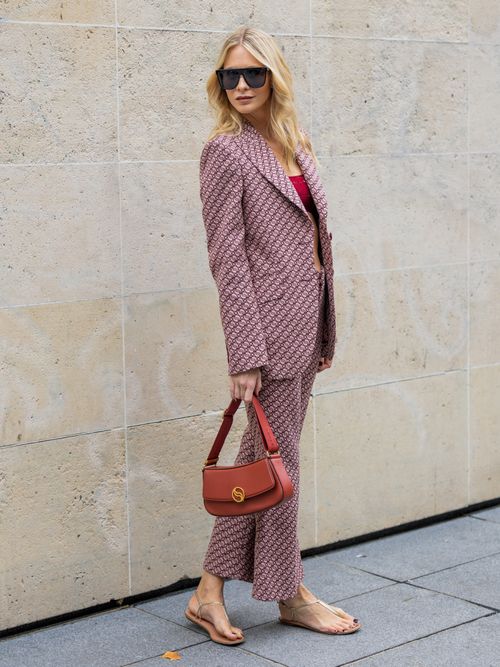 Poppy Delevingne trägt einen bunten Hosenanzug mit rotem Crop-Top und roter Tasche, dazu goldene Sandalen auf der Paris Fashion Week.