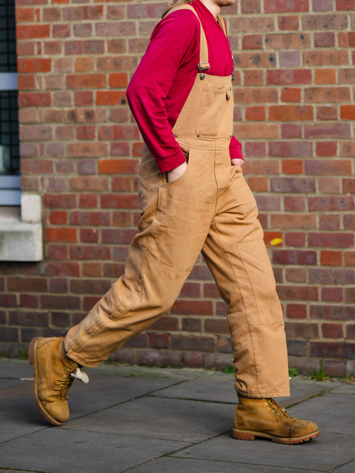 Street Style Look von der London Fashion Week, wo ein Gast eine beige Latzhose mit rotem Langarmshirt und Wander-Boots trägt.
