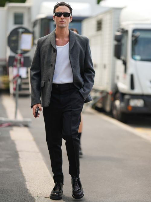 Street Style Look von der Milan Fashion Week, wo ein Gast eine graue Jacke, weißes T-Shirt, schwarze Jeans und eine schwarze Prada Brille trägt.