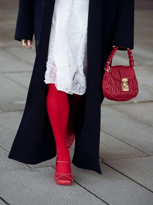 Miki Cheung wears red tights, red shoes, a red bag, a white dress, and a black coat outside Operasport during the Copenhagen Fashion Week AW24 on January 31, 2024 in Copenhagen, Denmark.