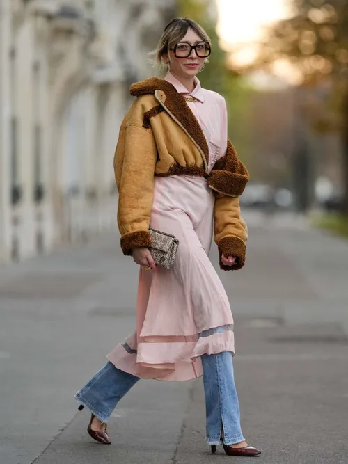 Emy Venturini trägt eine beige kurzgeschnittene Bomberjacke, ein rosafarbenes Blusenkleid mit einer Jeans darunter in Paris.