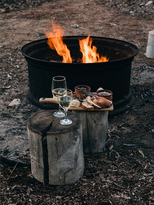Eine schwarze Feuerschale und davor zwei Baumstumpen mit einem Picknick.
