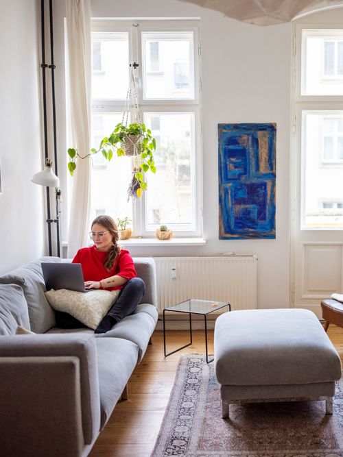 Foto von einem Wohnzimmer, wo eine Frau am Laptop arbeitet.