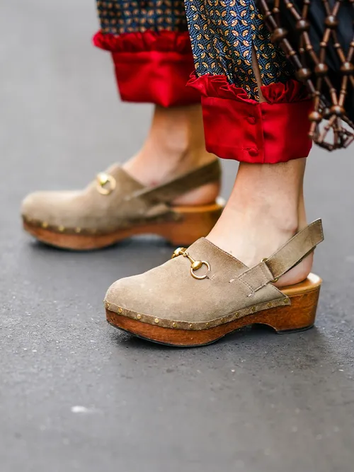 Close-up einer roten Seidenhose zu beigen Clogs aus Wildleder mit einer goldenen Schnalle.