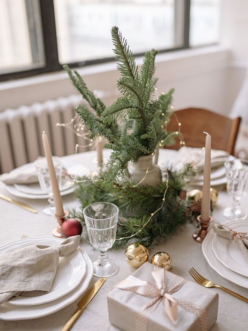 Runder Tisch mit einem Tannenzweig und Christbaumkugeln und weißen Tellern mit beigen Servietten.